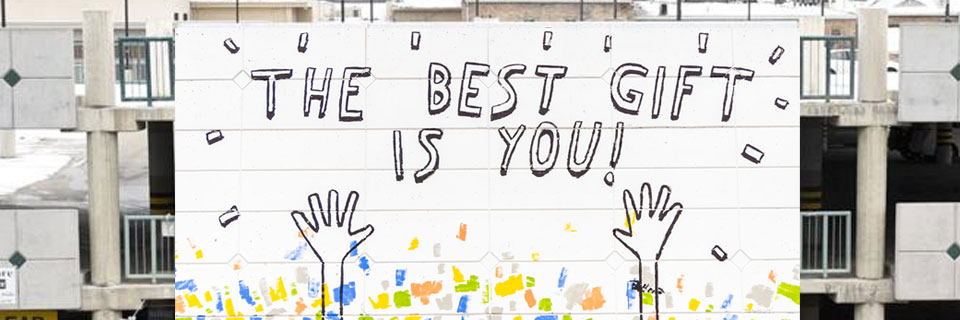 This is an image graphic of a wall mural created by Dallas Clayton, children’s author and artist from Los Angeles.
                         He, along with some help from little hands, painted a new mural on the parking structure at 52 N. 100 West,
                         entitled “The Best Gift is You.”
                         The message of the mural, Clayton said, is centered on self-acceptance and self-empowerment,
                         while also encouraging children to be a gift to someone else.